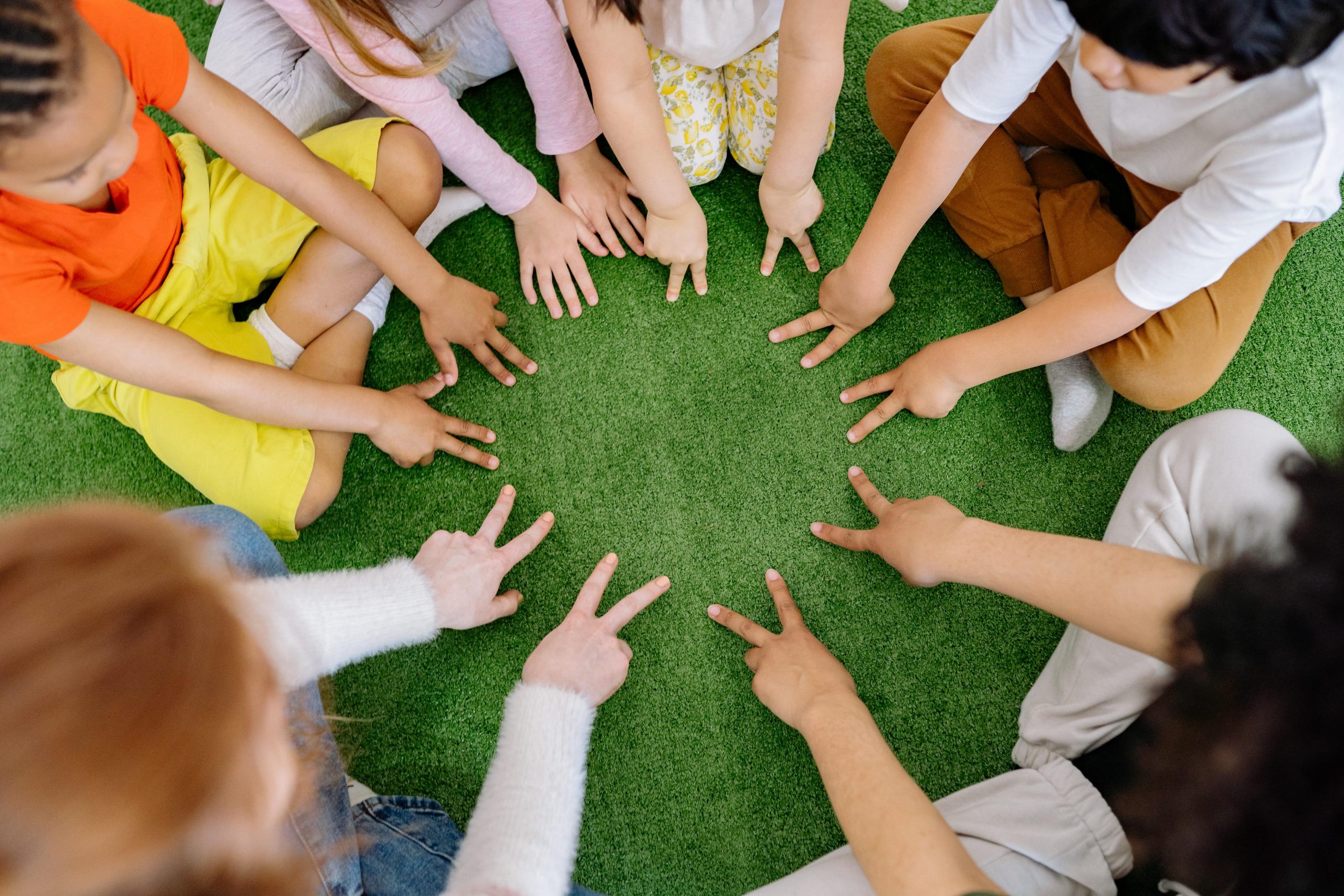 A circle of kids who have each placed two fingers into the circle.