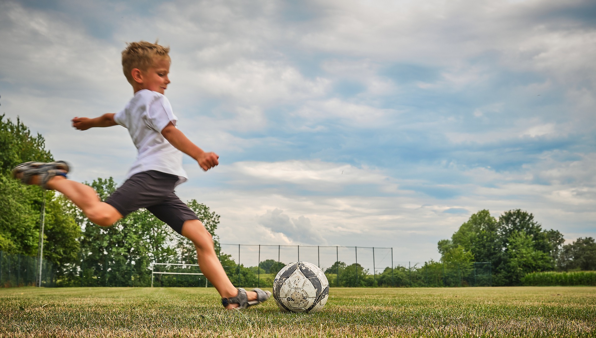 A young boy about to kick a football on a grass field.